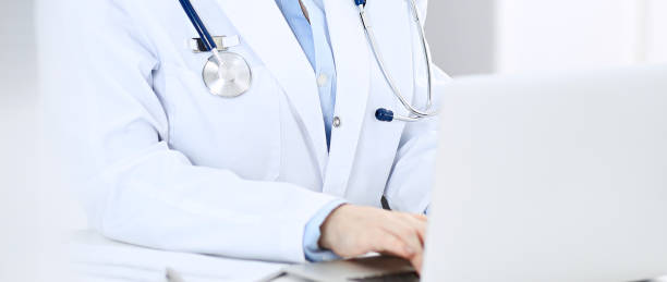 istock Doctor typing on laptop computer while sitting at the white table in hospital office. Physician at work. Medicine and healthcare concept 1127095312