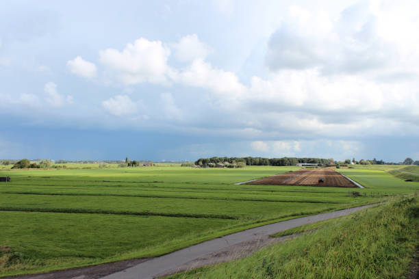 fields and meadows along dyke Hollandsche IJssel river with blue sky and white clouds. The polder behind the dyke is named zuidplaspolder and the lowest area in the Netherlands with 21ft below sea-level