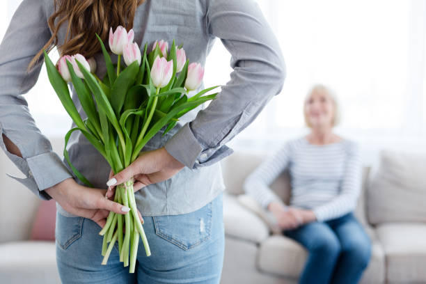 若い女性が彼女の母親の背中の後ろに花を持って - bouquet mothers day tulip flower ストックフォトと画像