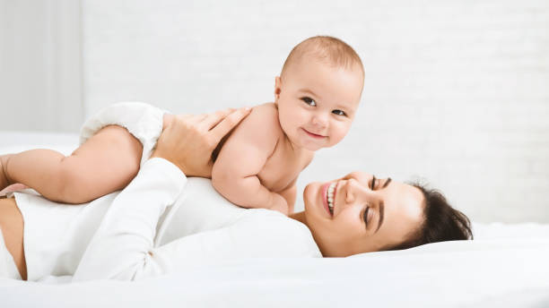 Mom and baby boy in diaper playing in bedroom Family having fun together. Mom and baby boy in diaper playing in bedroom, panorama, copy space cute baby laughing stock pictures, royalty-free photos & images
