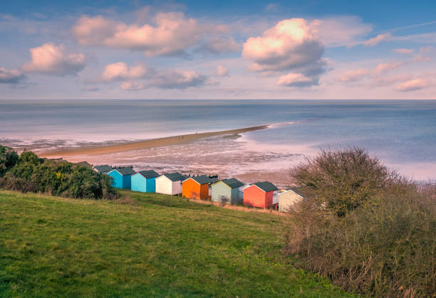 Impressive winter clouds in a cool blue sky over the beach huts and natural spit of land that stretches out to sea on the beach in Tankerton, Whitstable, Kent, UK. A three people are strolling on the natural and locally named 'Street' nubes de invierno impresionante en un cielo azul fresco en las playa cabañas y natural lengua de tierra que se extiende hacia fuera al mar en la playa de tankerton, whitstable, kent, reino unido. tres personas están paseando en la 'calle' natural y local