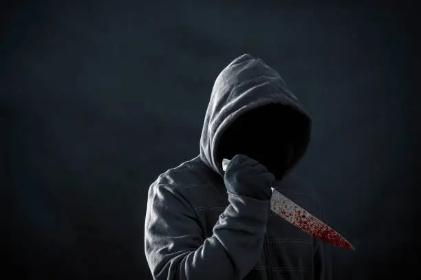 Photo of Hooded man with bloody knife in the dark