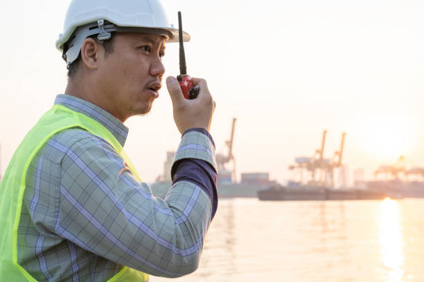 estivador de porto asiático, falando no rádio com o navio fundo - imagem - industrial ship dock worker engineer harbor - fotografias e filmes do acervo