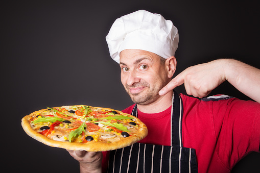 Portrait of happy attractive cook with a pizza in studio an a black background