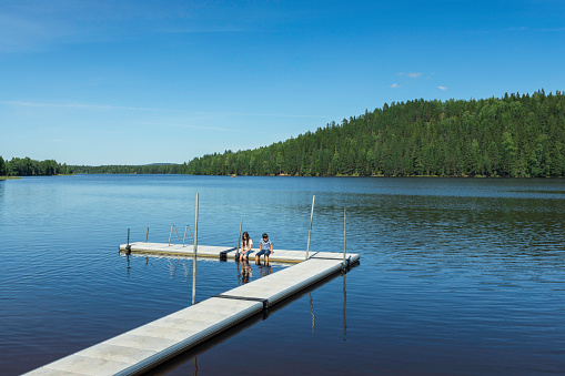 Two children sitting on a jetty in a lake in summer in Dalarna, Sweden.