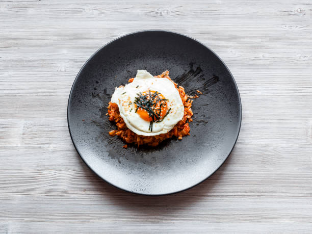 korean cuisine - top view of Kimchi bokkeum bap (fried rice with kimchi, beef and fried egg) on black plate on wooden board