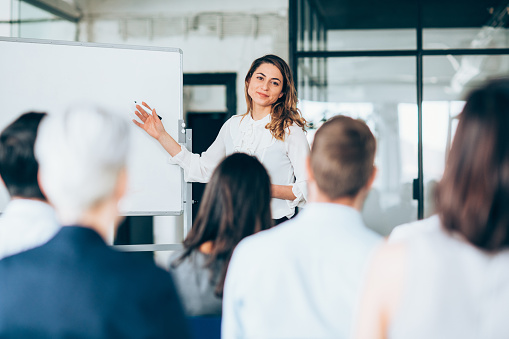 The young adult female university student nervously stands at the front of the class to present her project.