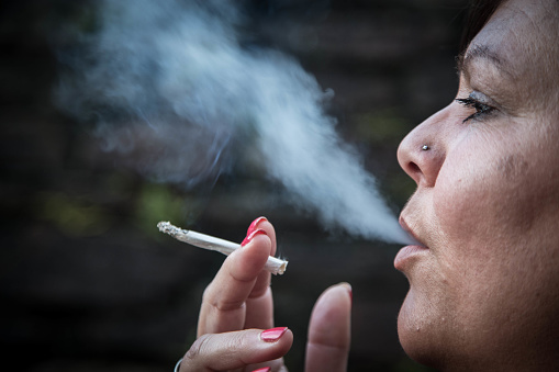 Profile of beautiful mature woman blowing out cigarette smoke