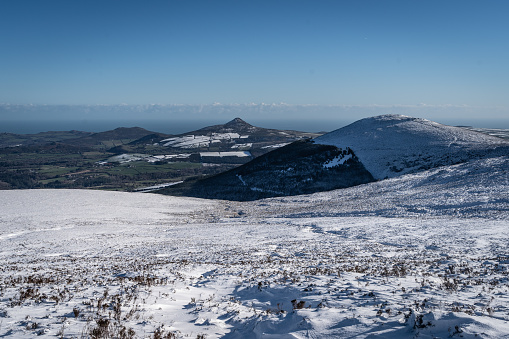 Wild beautiful barren landscape popular for hiking and walking trails covered in drifted snow in winter with distant Sugarloaf mountain and green lowlands with low sunshine with blue sky, the nearest mountain is Maulin, the Wicklow mountains, Ireland