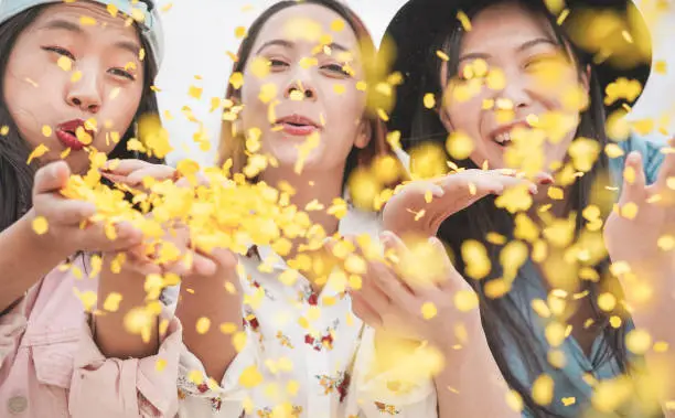 Happy asian friends having fun throwing confetti at party outdoor - Young trendy people enjoying fest event - Hangout, friendship, trends and youth concept - Focus on left girl face