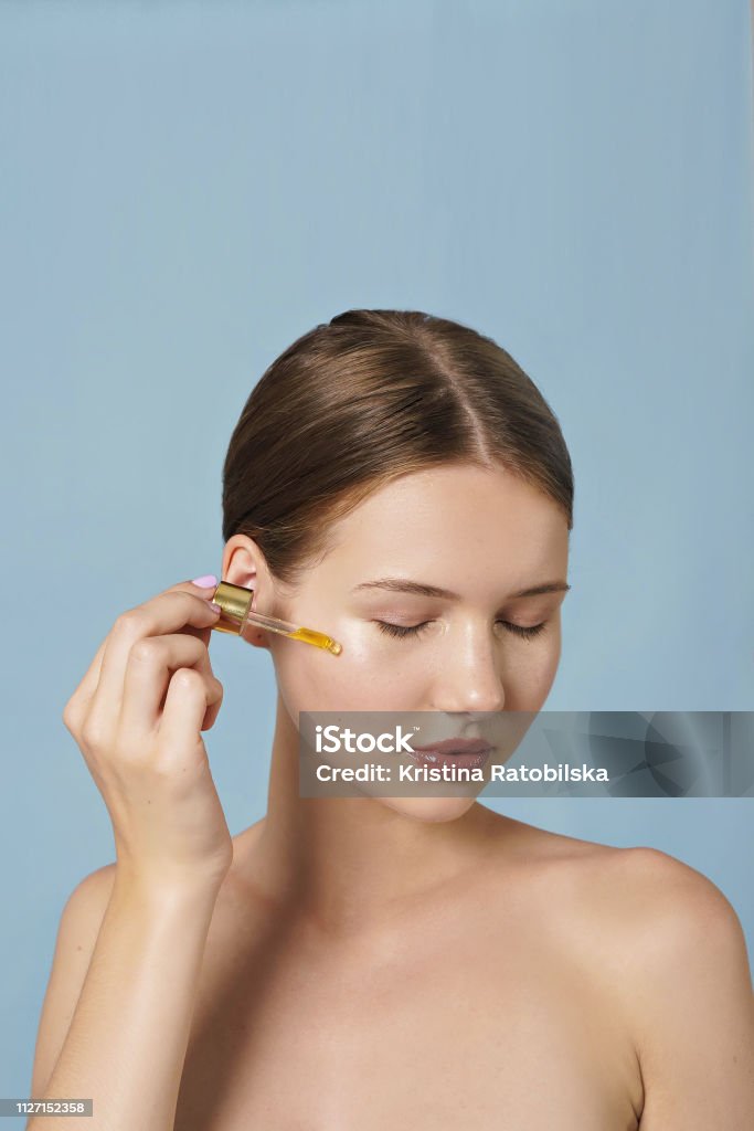attractive young woman beauty portrait , skin care concept portrait of young woman applying serum on her face on blue background Blood Serum Stock Photo