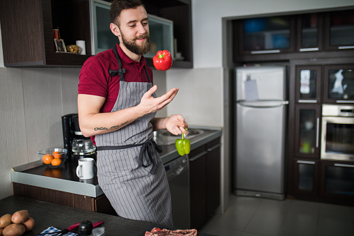 handsome man throwing pepper into air. guy preparing food at kitchen counter