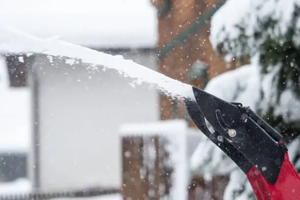 Someone uses a snowthrower outdoors in winter while it is snowing