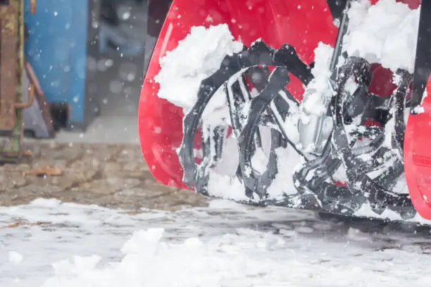 Someone uses a snowthrower outdoors in winter while it is snowing