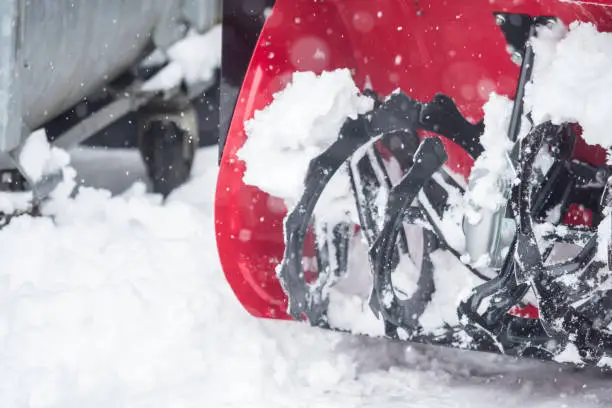 Someone uses a snowthrower outdoors in winter while it is snowing