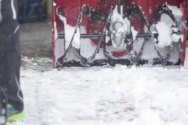 Someone uses a snowthrower outdoors in winter while it is snowing