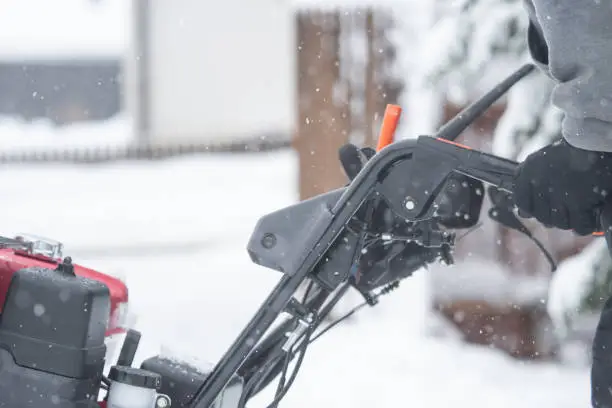 Someone uses a snowthrower outdoors in winter while it is snowing