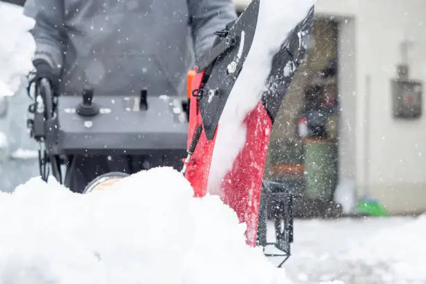Someone uses a snowthrower outdoors in winter while it is snowing