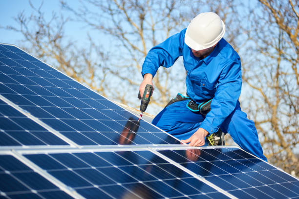 Electrician mounting solar panel on roof of modern house Male engineer in blue suit and protective helmet installing photovoltaic panel system using screwdriver. Professional electrician mounting solar module on roof. Alternative energy ecological concept. solar panel stock pictures, royalty-free photos & images