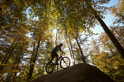 Young male cyclist riding on trial bicycle, rider making acrobatic trick on big boulder in the forest outdoor on summer sunny day. Concept of extreme sport active lifestyle