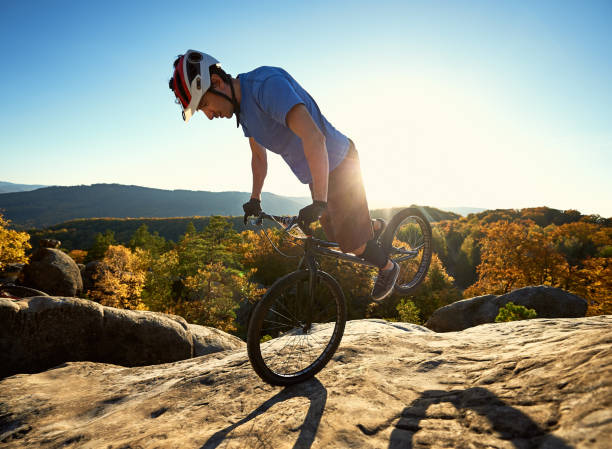 istock Cyclist balancing on front wheel on trial bicycle on boulder 1127160702