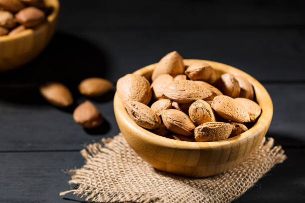 istock Almonds with shell in wooden bowls on slate background 1127161076