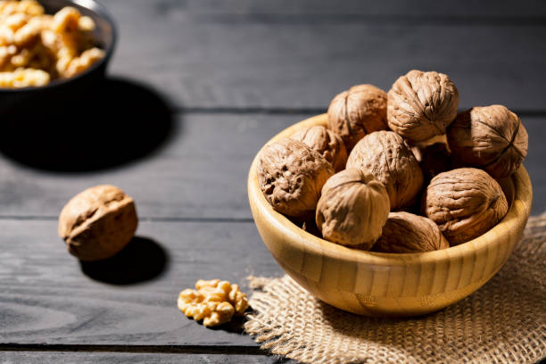istock Nuts with shell in wooden bowls on slate background 1127161139