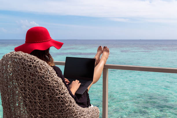 熱帯先のコンピューターで作業して赤い帽子を持つ若い女性 - on beach laptop working ストックフォトと画像