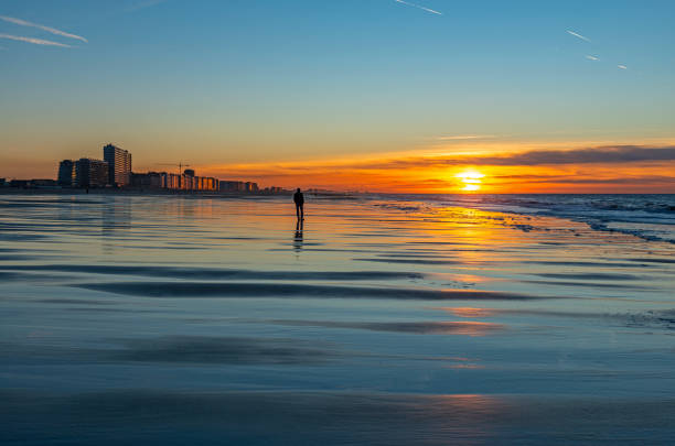 The beach of Ostend city and its skyline together with a silhouette of a person at sunset, West Flanders, Belgium.