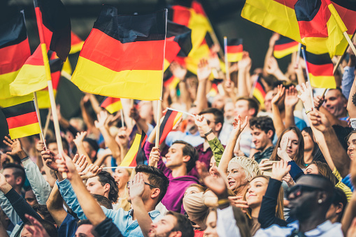 Large group of people waving Germany flags while standing on stadium bleachers.