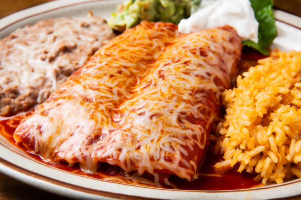 Enchiladas Rojas (Two chicken enchiladas topped with red sauce) Two chicken enchiladas topped with delicious red sauce. Garnished with guacamole and sour cream. enchilada stock pictures, royalty-free photos & images