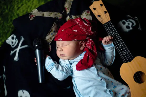 Photo of baby in a rocker bandana lies with a guitar and a microphone