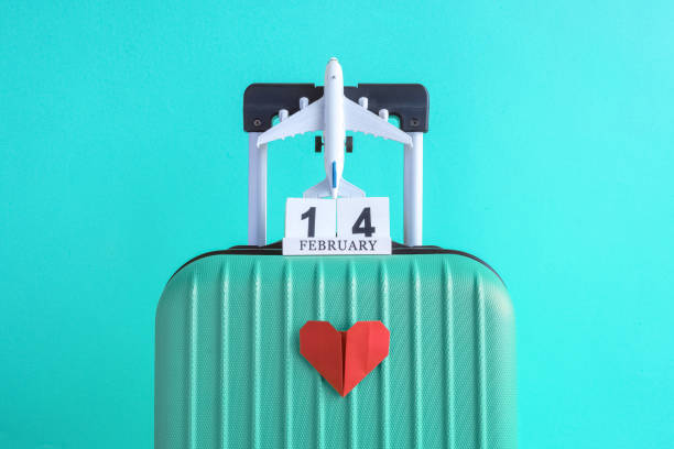 Luggage with valentines day date calendar and aircraft with paper heart on turquoise background minimalistic vacation concept. Suitcase with 14 of february wooden calendar and airplane model toy with origami red heart on light blue background minimal creative travel concept. valentines day holiday stock pictures, royalty-free photos & images