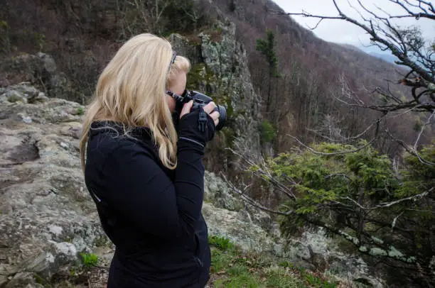 Blonde photographer takes photos with a DSLR camera of nature inside of Shenandoah National Park on an overcast day