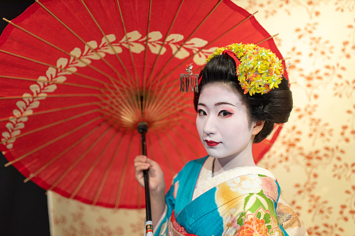 Maiko (Geisha in training) holding paper umbrella and looking at camera