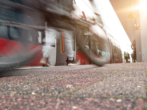 rail platform with red commuter train in motion blur, man with mike blurred in foreground