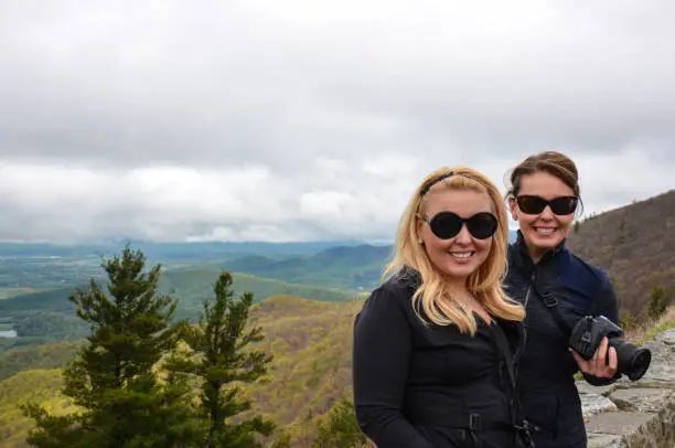 Two woman hikers pose on Stony Man Mountain on a foggy day in Shenandoah National Park. Concept for female friendship and travel