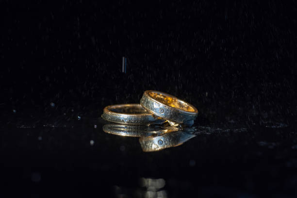 istock Wedding rings lying on dark surface shining with light close up macro. Water splashes 1127194947