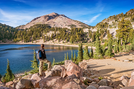 Stock photograph of hiker looking at view in Lassen Volcanic National Park on a sunny day, with Lake Helen and Lassen Peak in the background.