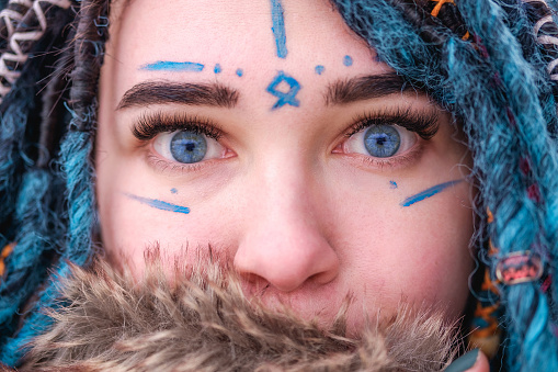 A girl with blue hair dreadlocks. Face painted with watercolors close up