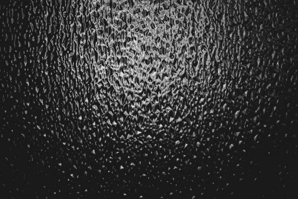 istock Corrugated window glass with light reflection in night. Atmospheric monochrome dark background. Shiny rippled glass glow in darkness close up. Detailed embossed texture in macro with copy space. 1127203149