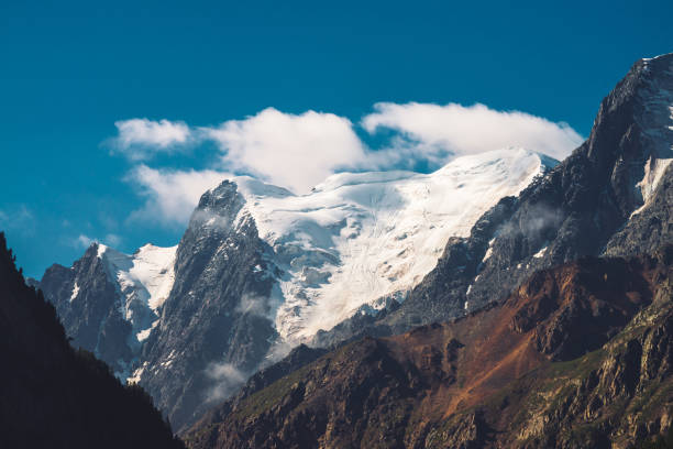 istock Low clouds and mist on top of mountain range. Glacier under clear blue sky. Snowy mountain peak in sunny day. Giant rocky ridge with snow. Atmospheric minimalist highland landscape of majestic nature. 1127203157