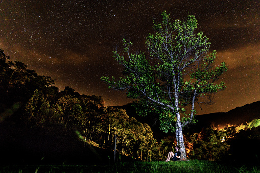 Young man sitting under a tree observing the stars