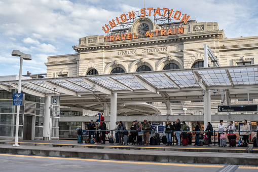 Passangers wait in line for Amtrak train in Union Station In Denver.  Union Station iconic sign is on the background.