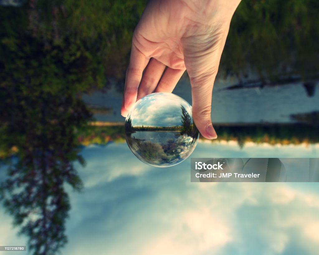 Image upside-down but right side up in glass crystal ball Hand holding crystal ball against horizon, and parklands of Maine Sphere Stock Photo