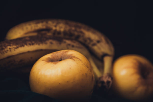 Overripe Bananas and Apples Against A Black Background stock photo