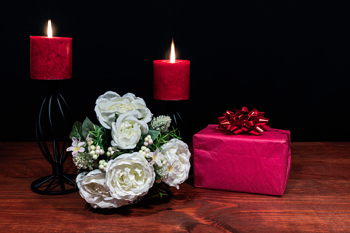 Beautiful bouquet of arranged flowers red candles on a holder with a present on a wooden table. mothers day, Easter, valentines, birthday, Christmas,