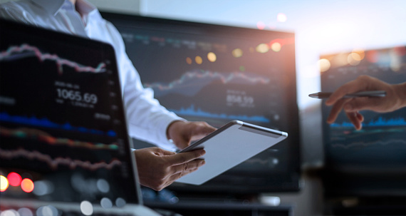 Business team working together. Businessman using tablet for analyzing data stock market in monitoring room with team pointing on the data presented in the chart on screen, forex trading graph, stock exchange trading online, financial investment concept. All on laptop screen are design up.