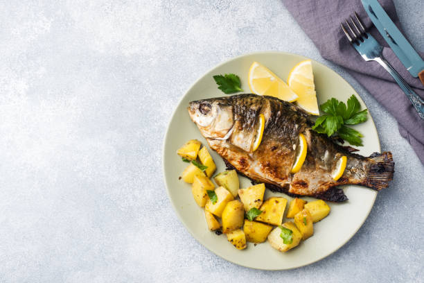 An oven roasted trout in a casserole on a rustic table. With carrots and potatoes on the side.