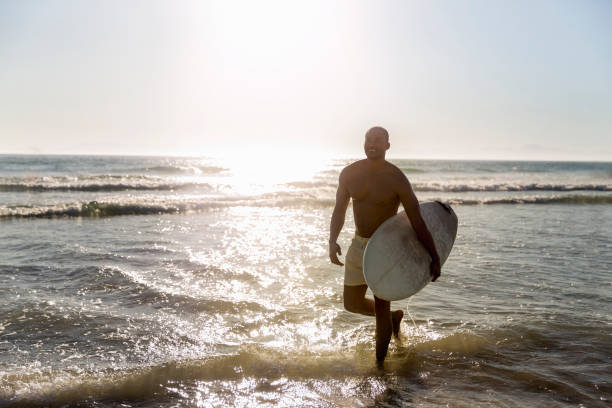 istock Smiling man carrying surfboard at beach 1127250561